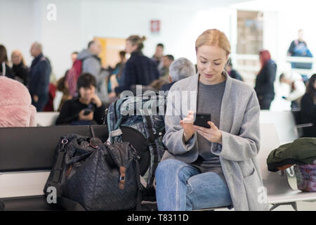 Viaggiatori femmina con il suo telefono cellulare mentre si è in attesa di salire a bordo di un aereo a cancelli di partenza al terminal aeroportuale. Foto Stock