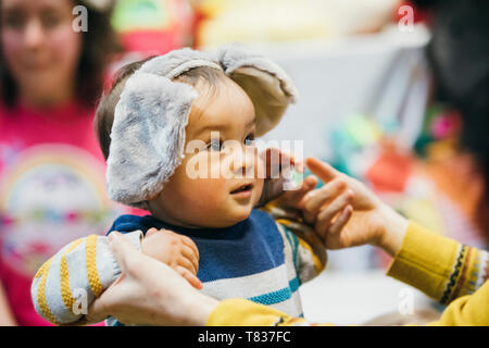 Immagine ravvicinata di un bambino tenuto da sua madre mentre indossa la novità delle orecchie. Foto Stock