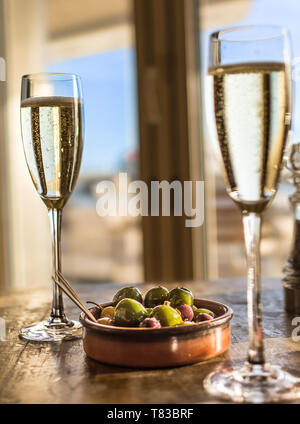 Bicchiere di champagne con una ciotola di olive miste su un tavolo di legno da una finestra nel ristorante sul mare Foto Stock