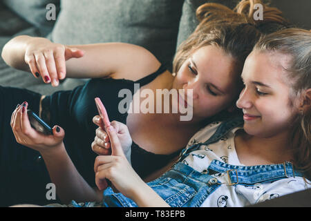 Giovani donne che utilizzano i telefoni cellulari guardare clip musicale, SMS, messaggistica. Gli adolescenti utilizzando gli smartphone, seduto sul divano di casa. Utilizzando la tecnologia de Foto Stock