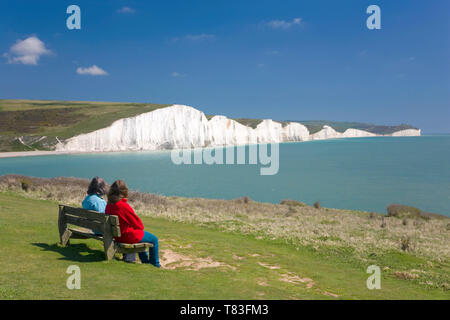 Cuckmere Haven, East Sussex, Inghilterra. I visitatori su banco ammirando vista su tutta la baia da Seaford testa per le Sette Sorelle scogliere. Foto Stock