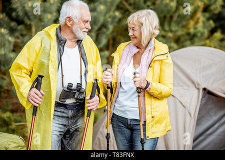 Coppia senior in giallo impermeabili in piedi presso il campeggio con la tenda nel giovane pineta Foto Stock