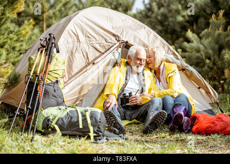 Coppia senior in giallo raincoats seduti insieme vicino alla tenda presso il campeggio nel bosco Foto Stock