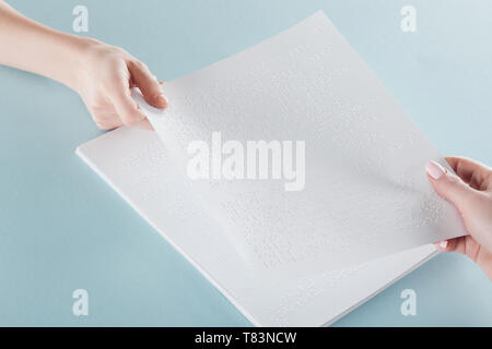 Vista ritagliata della giovane donna tenendo la carta con testo braille isolato su blu Foto Stock