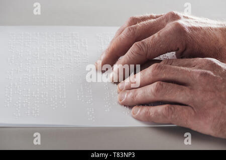 Vista parziale di senior uomo la lettura di testo braille isolato su grigio Foto Stock