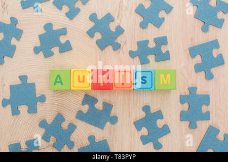 Vista dall'alto di autismo scritte fatte di cubi variopinti tra puzzle blu pezzi sul tavolo di legno Foto Stock