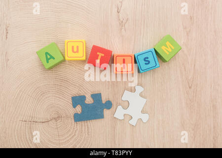 Vista dall'alto di autismo scritte fatte di cubi variopinti vicino a pezzi di un puzzle sul tavolo di legno Foto Stock