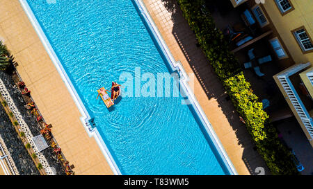 Top vista verticale della piscina in hotel residence vacanza con persone adulti senior stabiliscono e godere con gonfiabili materassini gonfiabili materasso su blue wat Foto Stock