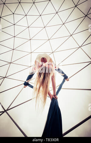 Punto di vista alternativo della bella bionda ragazza caucasica antenna facendo circus sport show con esercizi di cielo bianco in background - caldo colore giallo Foto Stock