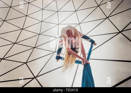 Punto di vista alternativo della bella bionda ragazza caucasica antenna facendo circus sport show con esercizi di cielo bianco in background - caldo colore giallo Foto Stock