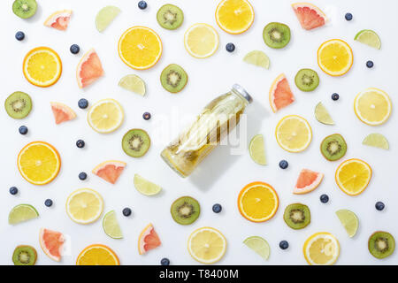 Vista dall'alto di detox drink in bottiglia tra fette di frutta e mirtilli su sfondo bianco Foto Stock