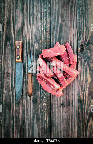 Non cotti materie carni bovine disossate di nervature con carne di vintage forchetta e coltello da macellaio sopra la parte superiore di una tavola in legno rustico / background. Immagine ripresa dalla vista aerea. Foto Stock