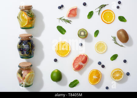 Vista dall'alto di detox drink in vasi vicino a fette di frutta, mirtilli, menta e rosmarino Foto Stock