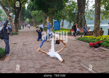 Una giovane coppia eseguire acrobazie sul marciapiede sul lato del Lago Hoan Kiem nel centro storico di Hanoi, Vietnam del nord e del sud-est asiatico Foto Stock