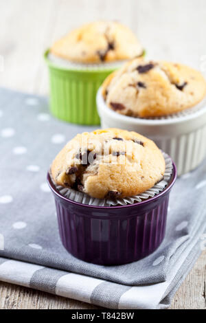 Tre fatti in casa muffin freschi su ceramiche colorate bocce su lino tovaglioli su tavola in legno rustico sfondo. Foto Stock