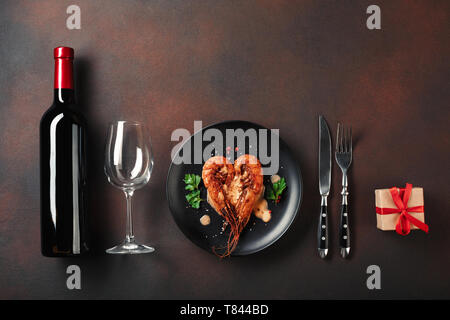 Cena romantica con a forma di cuore di gamberetti e vino su uno sfondo di colore marrone. Vista da sopra con copia spazio. Foto Stock