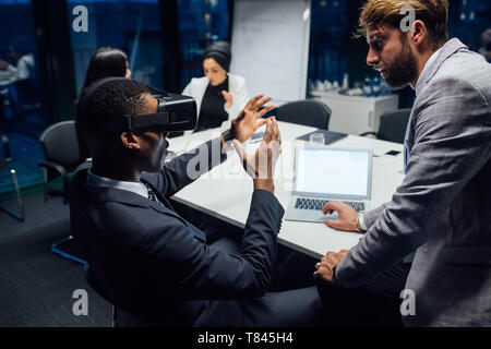 Imprenditore cerca attraverso la realtà virtuale cuffia durante un tavolo per conferenza incontro Foto Stock