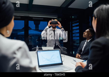 Imprenditore cerca attraverso la realtà virtuale cuffia durante un tavolo per conferenza incontro Foto Stock