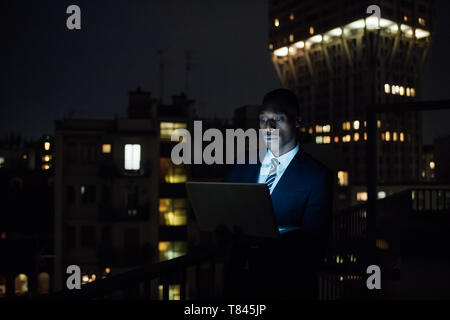 Giovane uomo d affari con computer portatile sul balcone per ufficio di notte Foto Stock