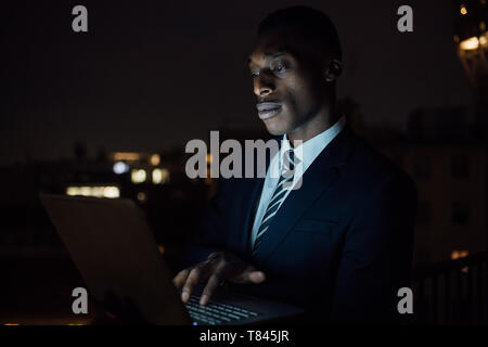 Giovane imprenditore digitazione sul computer portatile sul balcone per ufficio di notte, vicino fino Foto Stock