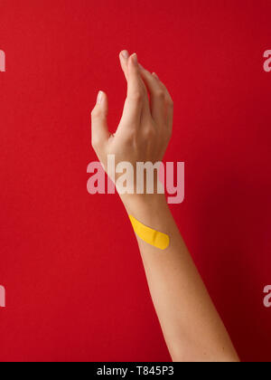 Primo soccorso cerotto sulla donna di polso contro lo sfondo rosso Foto Stock