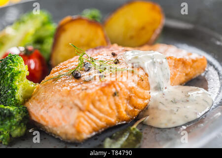 Arrosto di filetto di salmone broccoli pomodori e patate fritte con aneto salsa alla panna Foto Stock