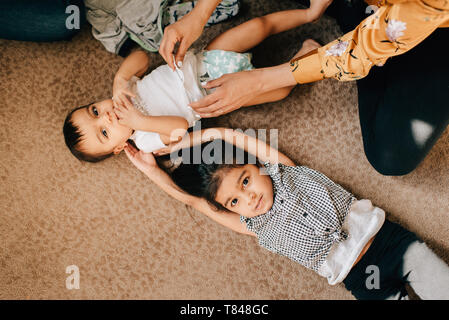 Ragazza distesa sul pavimento di vivaio mentre madre modifica baby fratello del pannolino, overhead ritratto Foto Stock