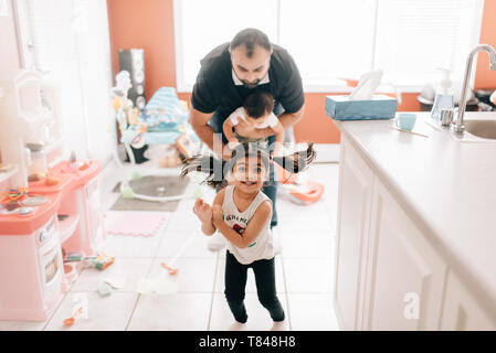 Ragazza che gioca in cucina nella parte anteriore del padre e fratello di bambino, ritratto Foto Stock