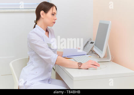 Medico di concentrato con relazione guardando il monitor di un computer alla scrivania in ufficio medico. Foto Stock
