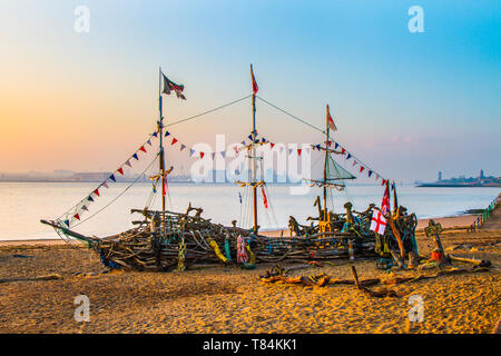 Pirata Barca Alba sul fiume Mersey, skyline del centro città, scultura in legno, banchine e porto. La Black Pearl è un'opera d'arte interattiva in legno di driftwood creata e mantenuta da un piccolo gruppo di pirati appassionati sulla riva di New Brighton. Una replica di un pirata a tre alberi uomo di guerra, è quasi interamente costruito da materiali recuperati, rottami, rifiuti, smaltimento, roba, Relitto, attrezzature, materie prime, opere d'arte ambientali in legno di driftwood trovate sulla spiaggia di Liverpool Merseyside. Foto Stock