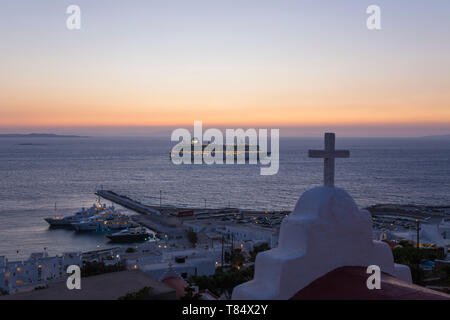 La città di Mykonos, Mykonos, Egeo Meridionale, Grecia. Vista sul mare Egeo dalla collina, crepuscolo, illuminato nave da crociera ancorata al largo. Foto Stock