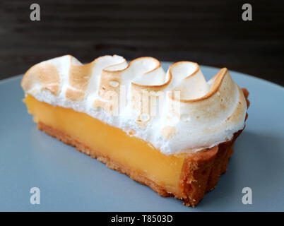 Primo piano una fetta di succulenti Lemon Meringue Tart su una piastra di colore blu Foto Stock