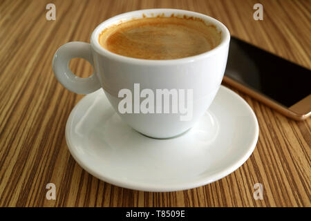 Una tazza calda di caffè nero con un Smartphone sfocate in background Foto Stock