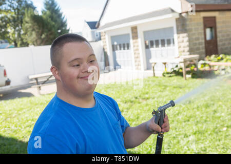 Teen con la sindrome di Down che porta tubo da giardino Foto Stock