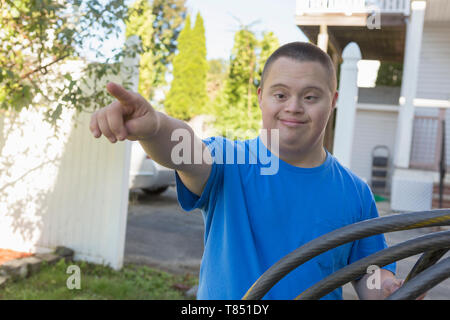 Teen con la sindrome di Down che porta tubo da giardino Foto Stock