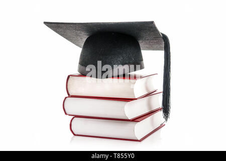 Graduazione nera hat sulla pila di tre hard cover libri su bianco Foto Stock