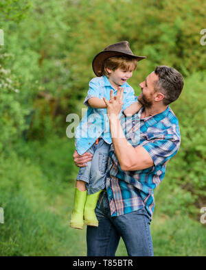 Eco farm. piccolo bambino aiutare il padre in agricoltura. il padre e il figlio nel cappello da cowboy sul ranch. kid in stivali di gomma. uomo felice papà nella foresta. natura e uomo. il giorno della famiglia. felice giornata della terra. famiglia felice. Foto Stock