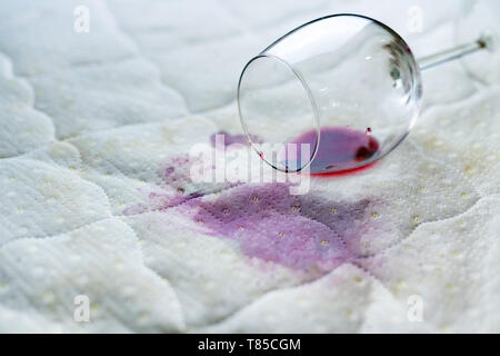 Eventuali fuoriuscite di vetro del vino sul letto. Caduta accidentale wineglass sul lenzuolo bianco. Sfortunato, spiacevole situazione. Macchia di bagnato. Foto Stock