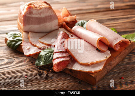 Tavola di legno con gustose fette di deliziosi affettati su tavola Foto Stock