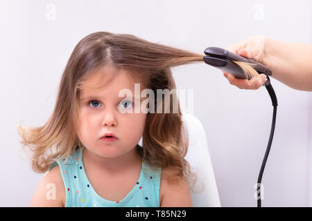 Madre stiratura dei capelli con la piastra per capelli a sua figlia Foto Stock