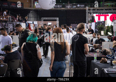 Si vedono persone a piedi e guardare il tatuaggio gli artisti fanno il loro lavoro durante il festival. Migliaia di tatuaggio di artisti di tutto il mondo hanno preso parte nel corso della XIII Athens International Tattoo Convention e hanno anche fatto tatuaggi a coloro che erano interessati. Foto Stock