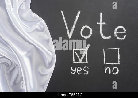 Vista dall'alto di voto scritte e segno di spunta vicino a sì parola sulla lavagna nera vicino a bandiera bianca Foto Stock