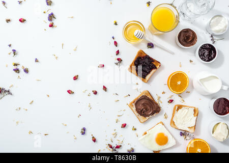 Vista dall'alto di toast e marmellata e uovo fritto nei pressi di bicchieri di acqua e succo di arancia su bianco Foto Stock