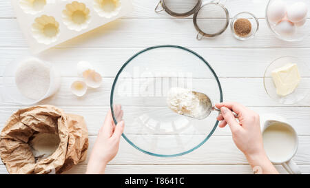 Vista ritagliata della donna con convogliatore di mettere la farina in un recipiente durante la cottura sul tavolo Foto Stock