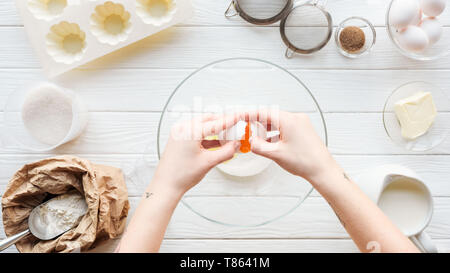 Vista parziale di donna uovo di cracking nel recipiente durante la cottura sul tavolo di legno Foto Stock