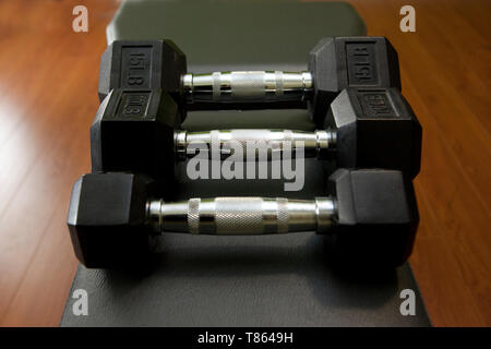 Tre piccoli manubri di peso su una panca con un rack di dumbell in background Foto Stock