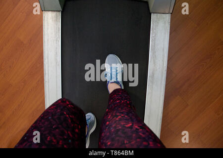 Guardando verso il basso in corrispondenza di una coppia di gambe e sneakers pronto a correre su un tapis roulant Foto Stock