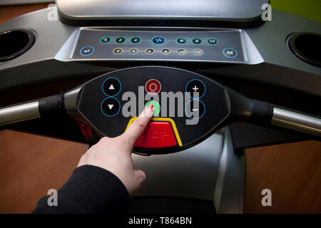 Preparati a correre- mano spinge il pulsante verde di avvio su un tapis roulant in una palestra di casa Foto Stock