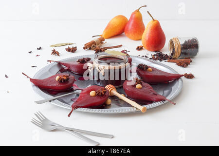 Hibiscus pere in camicia, dolce dessert di frutta. Vassoio in argento con pere, abbellito con nocciole, foglie di alloro, essiccati Fiori di ibisco, anice stelle, e Foto Stock