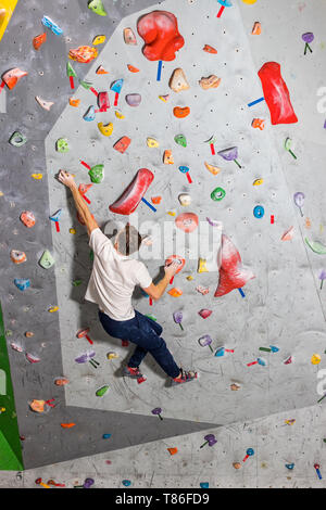 Rocciatore uomo appeso su un bouldering parete di arrampicata, all'interno sui ganci colorati Foto Stock